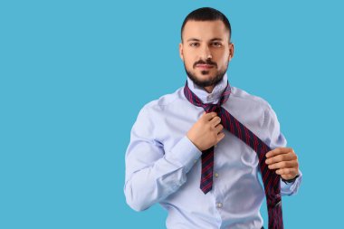 Genç işadamı mavi arka planda kravat bağlıyor