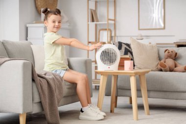 Evdeki kanepede elleri ısıtan küçük bir kız.