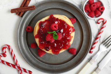 Ahududu reçelli bir tabak tatlı krep ve beyaz arka planda Noel şekerleri.