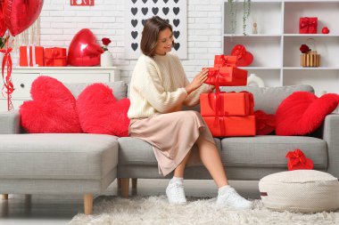 Oturma odasındaki kanepede hediye kutularıyla oturan güzel genç bir kadın. Sevgililer Günü kutlaması