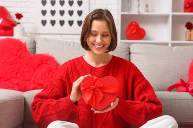 Oturma odasında hediye kutusu olan mutlu genç bir kadın. Sevgililer Günü kutlaması