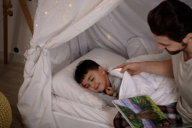 Baba, küçük oğluna masal okuyor. Kulübede uyuyor.