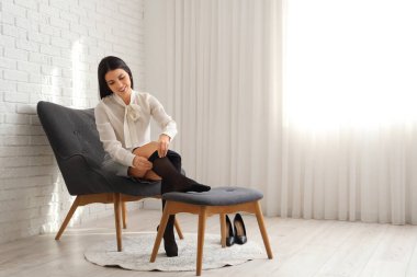 Genç bir kadın koltuğunda otururken siyah tayt giyiyor.