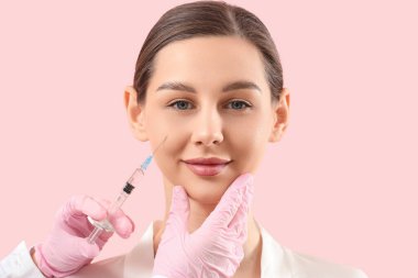 Genç kız pembe arka planda yüzüne enjeksiyon yaptırıyor.