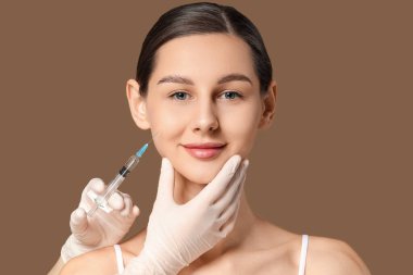 Genç kız kahverengi arka planda yüzüne enjeksiyon yaptırıyor.