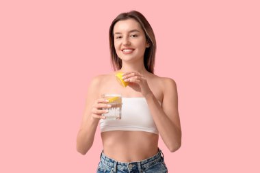 Güzel genç bir kadın pembe arka planda limon sıkıyor.