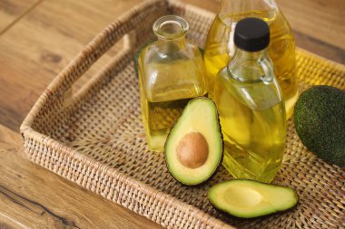 Taze yağ şişeleri ve ahşap arka planda avokado dolu hasır tepsi.