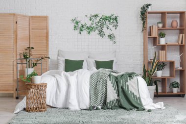 Yatak odasının içinde raf ünitesi, katlanır ekran ve yeşil bitkiler var.