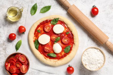 Beyaz grunge arka planda çiğ pizza ve malzemelerle yuvarlanan iğne.