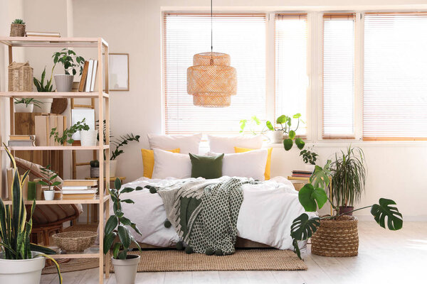 Interior of light bedroom with green plants and bookshelf