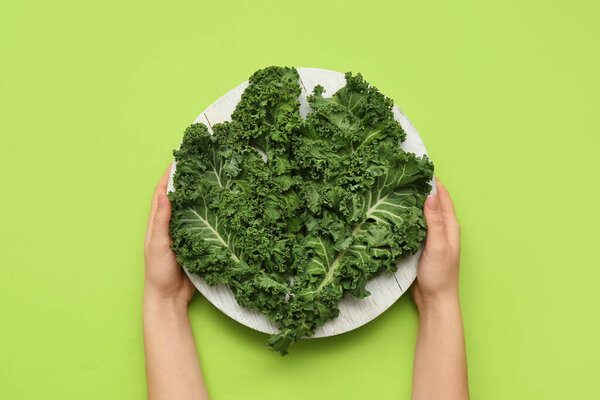 Female hands with white wooden board of fresh kale cabbage leaves on green background