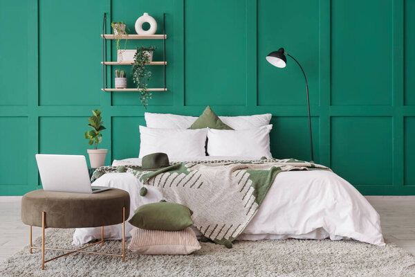 Интерьер спальни с лампой, полкой и ноутбуком на пуф