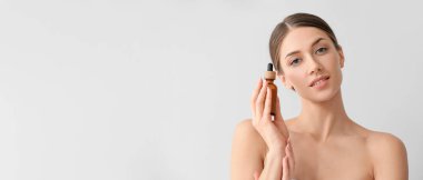 Güzel genç bir kadın hafif arka planda kozmetik serumu şişesi tutuyor ve metin için yeri var.