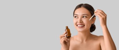 Güzel Asyalı kadın yüzüne kozmetik serumu uyguluyor.