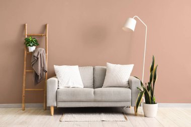 Yastıklı gri kanepe, oturma odasındaki bej duvarın yanında yer lambası ve merdiven.