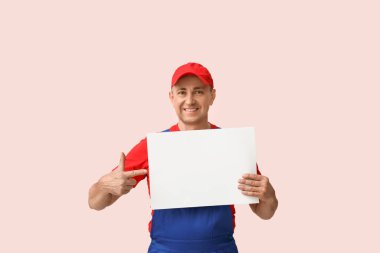 Erkek tamircinin portresi pembe arka plandaki boş postere işaret ediyor.