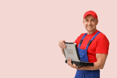 Pembe arka planda eski dizüstü bilgisayarı olan erkek tamircinin portresi