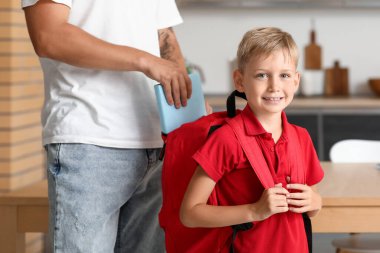 Baba evde oğlunun sırt çantasına kitap koyuyor.