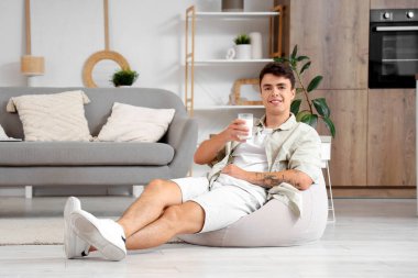 Evde bir bardak sütle oturan genç adam.