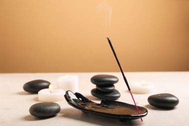Yanan tütsü çubuğu, yanan mumlar ve ışık masasında renk arkaplanına karşı spa taşlarıyla tutucu