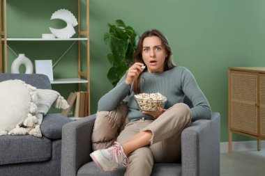 Patlamış mısırla şok olmuş genç bir kadın evdeki koltukta film izliyor.