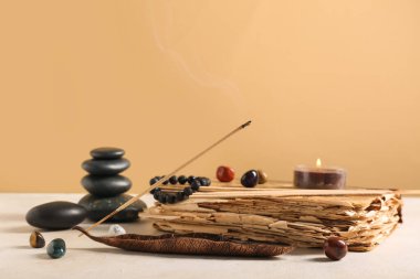 Renk duvarına karşı aromatik tütsü çubukları, eski kitap ve spa taşlarıyla kompozisyon