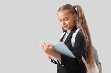 Okul üniformalı şirin küçük kız gri arka plan üzerine kitap okuyor.