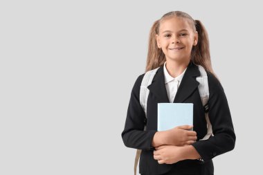 Okul üniformalı, gri arkaplanı olan şirin bir kız.