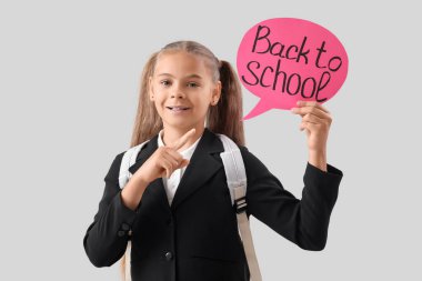 Okul üniformalı şirin kız, gri arka planda okula geri dönen mesajla konuşma baloncuğunu işaret ediyor.