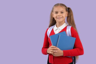 Okul üniformalı, leylak arkaplanıyla ilgili kitapları olan sevimli küçük bir kız.