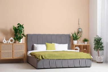 Yumuşak yataklı şık bir yatak odası, yeşil ekoseli, çekmeceli ve çiçekli bir sandık.