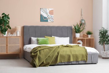 Yumuşak yataklı şık bir yatak odası, yeşil ekoseli, çekmeceli ve çiçekli bir sandık.