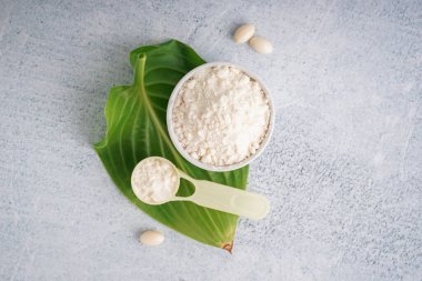 Bardak ve kepçe dolusu kolajen tozu ve beyaz grunge arka planda haplar.