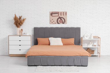 Şık bir yatak odası, yatak odası, çekmeceler, raf ünitesi ve vazo dolusu otlar.