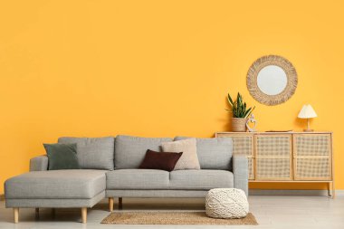 Sıcak kanepe, çekmeceler ve oturma odasındaki sarı duvardaki ayna.