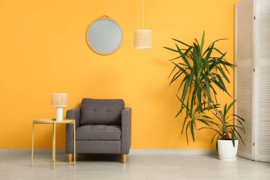 Koltuk, lamba, ayna ve odanın yanındaki sarı duvarlı kahve masası.