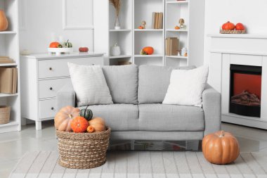 Oturma odasının içi gri kanepe, raf üniteleri, şömine ve farklı balkabaklarıyla dolu sepetlerle dolu.