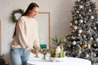 Genç bir kadın Noel arifesinde yemek odasına bardak koyuyor.