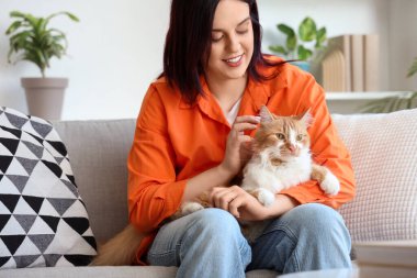 Evdeki kanepede oturan kedisi olan genç bir kadın.