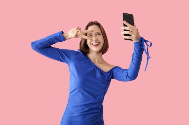 Cep telefonlu güzel bir kadın pembe arka planda selfie çekiyor.