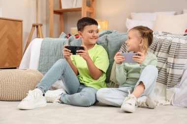 Cep telefonlu şirin çocuklar evde yerde video oyunu oynuyorlar.