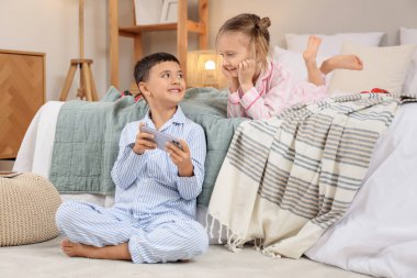 Evde pijamalı, cep telefonlu, video oyunu oynayan sevimli çocuklar.