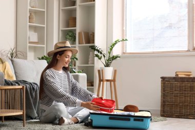 Evinde yerde oturan bavulu ve ilk yardım çantasıyla mutlu genç bir kadın. Seyahat kavramı