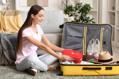 Evinde bavulu ve ilk yardım çantası olan mutlu genç bir kadın. Seyahat kavramı