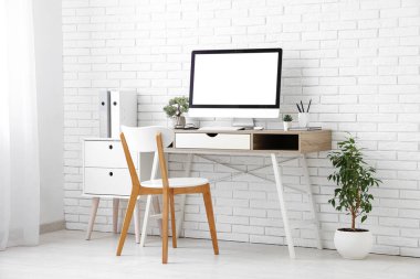 Işık ofisindeki beyaz tuğla duvarın yanında bilgisayar ve sandalye olan şık bir iş yeri