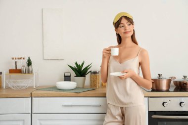 Pijamalı, evde kahve içen güzel, mutlu bir kadın.