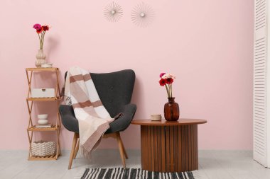 Koltuk, ekose, raf ünitesi ve vazoda Gerbera çiçekleri oturma odasının içindeki sehpanın üzerinde.