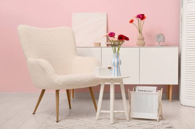 Koltuk, çekmeceler ve kahve masası. Oturma odasının içindeki vazoda Gerbera çiçekleri var.