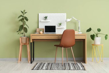 Boş dizüstü bilgisayarı, masa lambası ve yeşil duvarın yanında tahta tahtası olan şık bir iş yeri. Serbest konsept