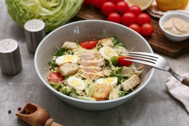 Lezzetli tavuklu Sezar salatası ve gri arka planda malzemeler, yakın plan.